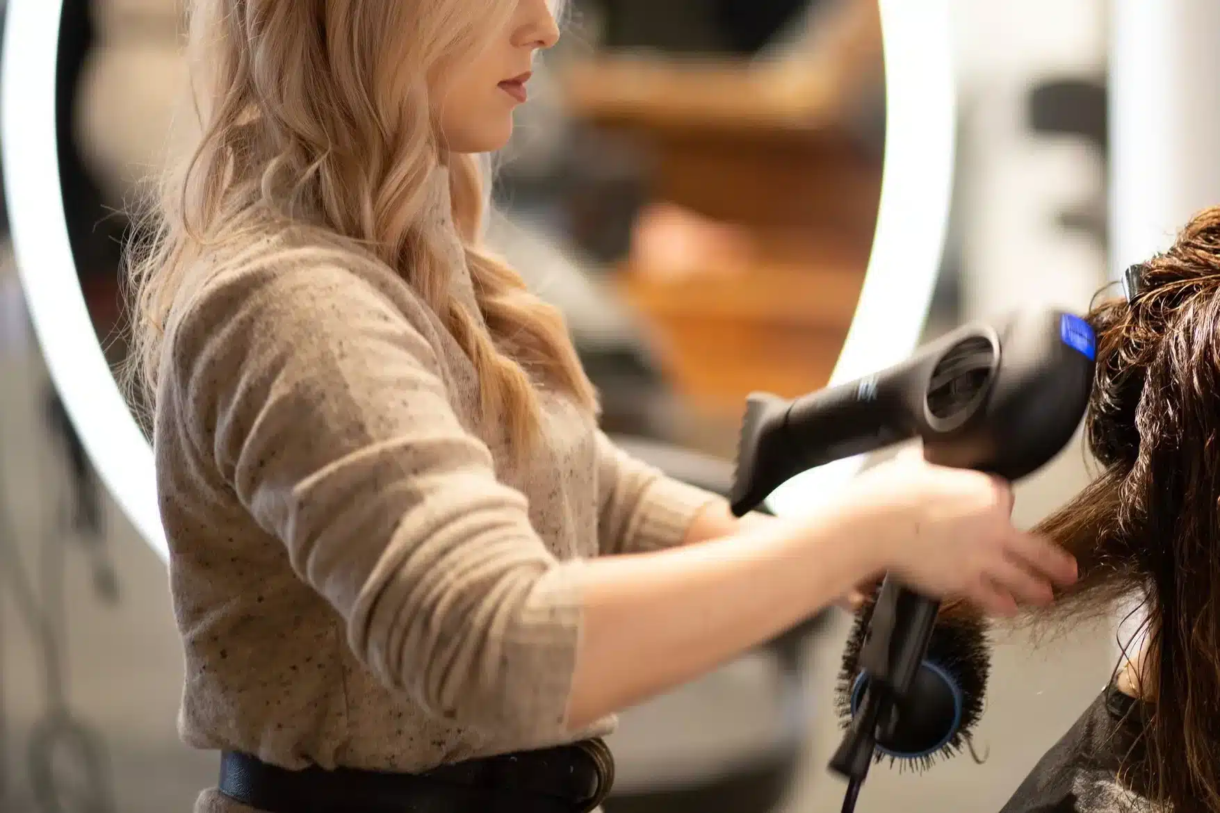 A hairstylist drying a client's hair with a handheld blow dryer.