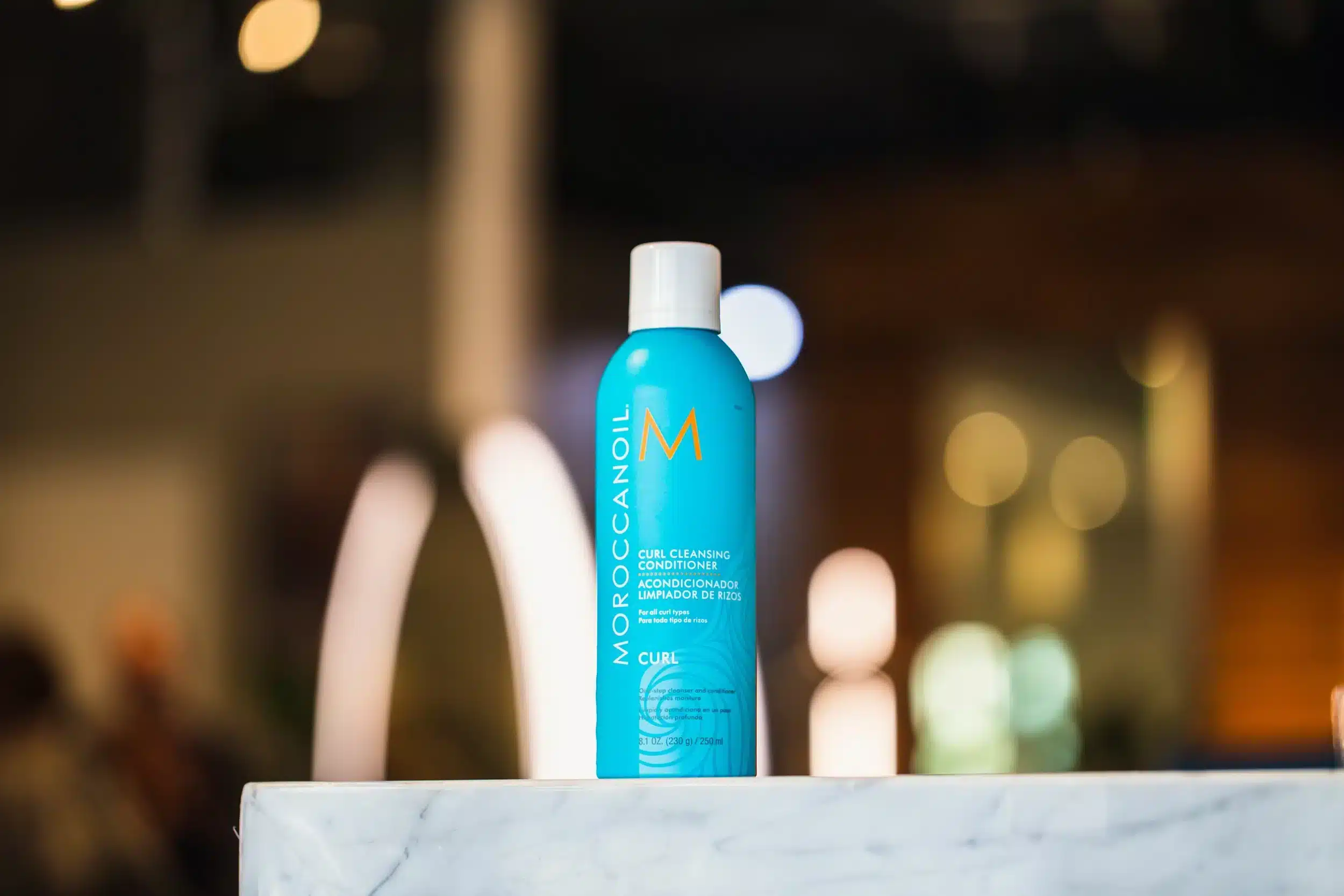 Bottle of Moroccanoil Curl Cleansing Conditioner on marble surface with blurred background.