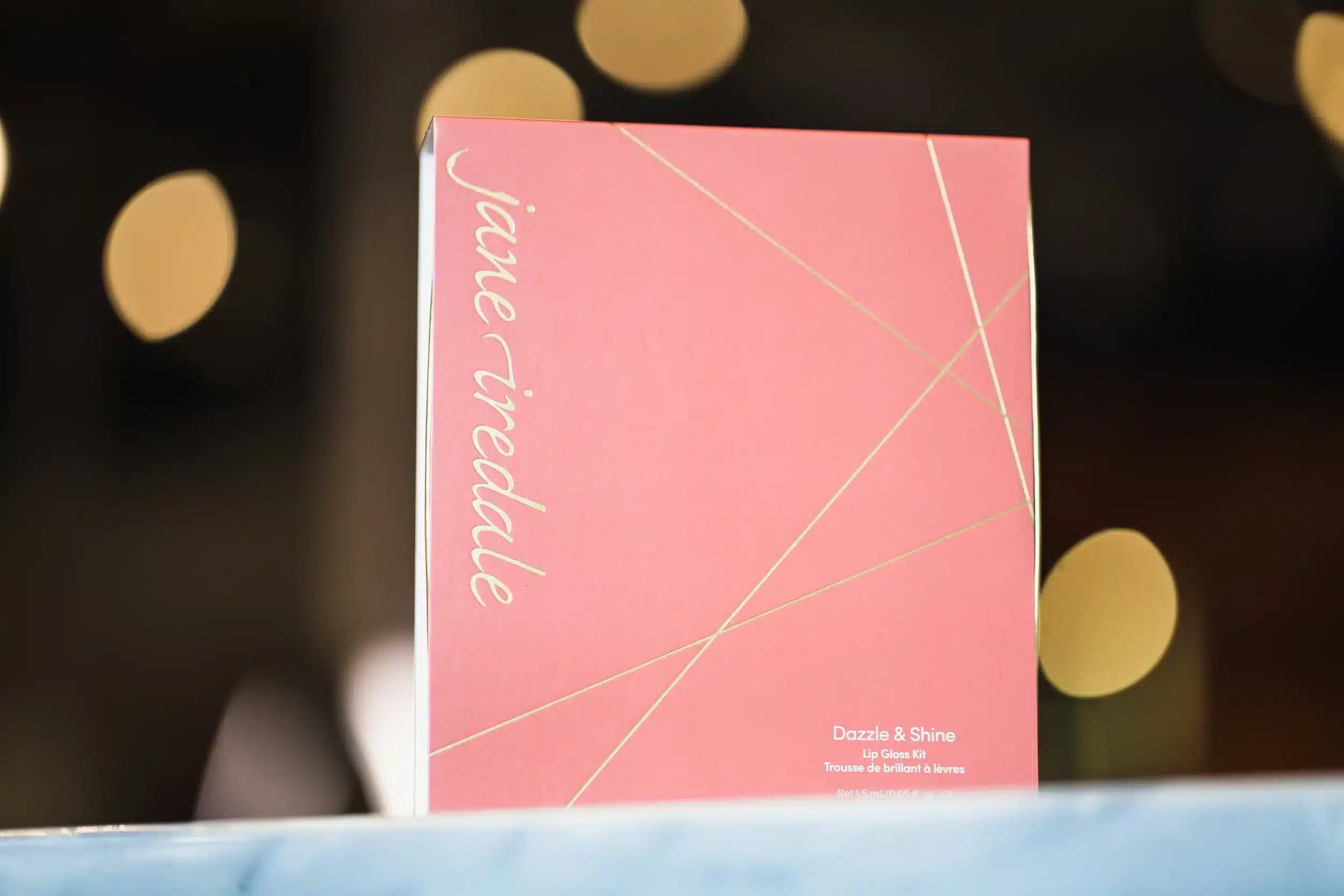 Jane Iredale Dazzle & Shine Lip Gloss Kit with pink and gold packaging against a blurred background.